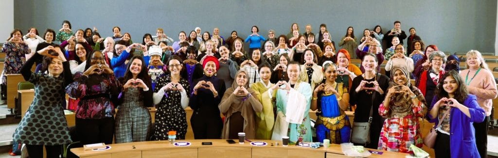 A big group of women at man event making heart hand gestures. 