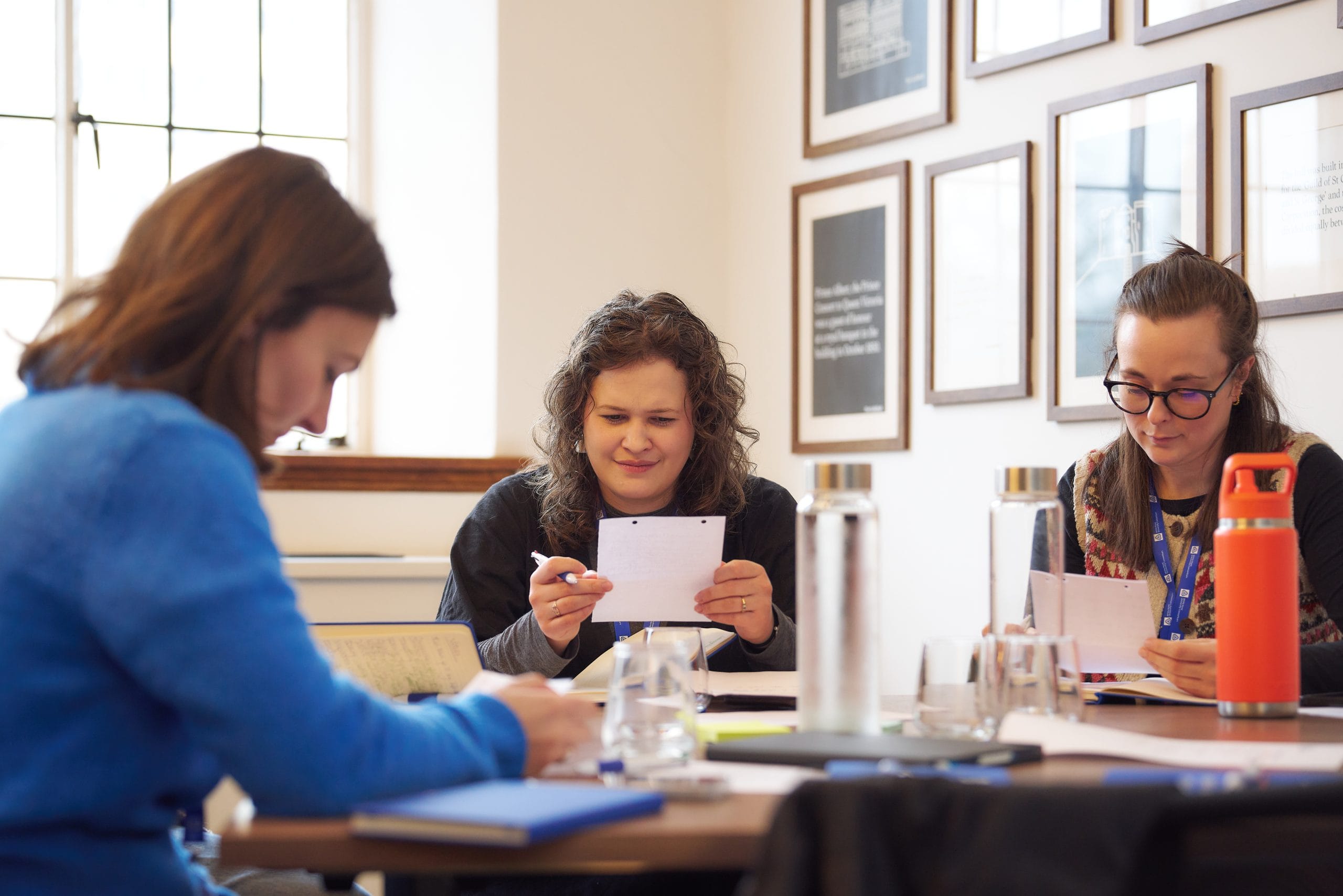 3 women sat around table reading pieces of paper