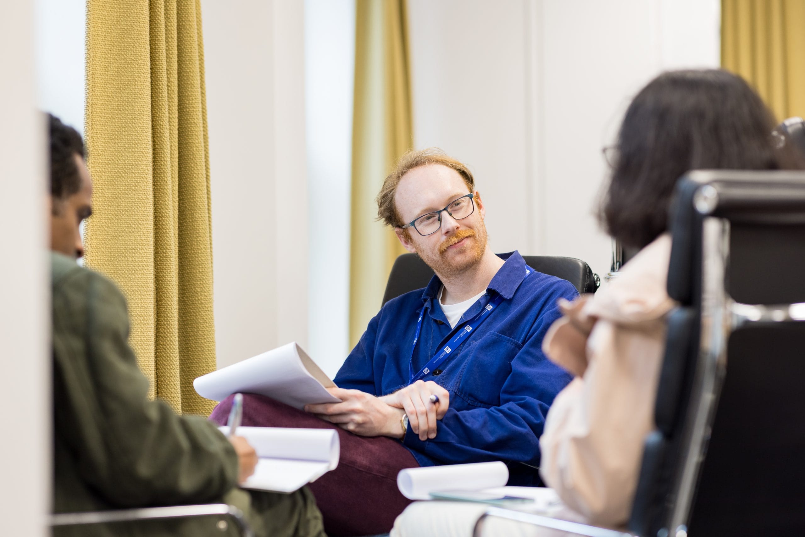 Man with glasses and White Rose Univesrity Consortium lanyard listens to a woman (facing away from camera).