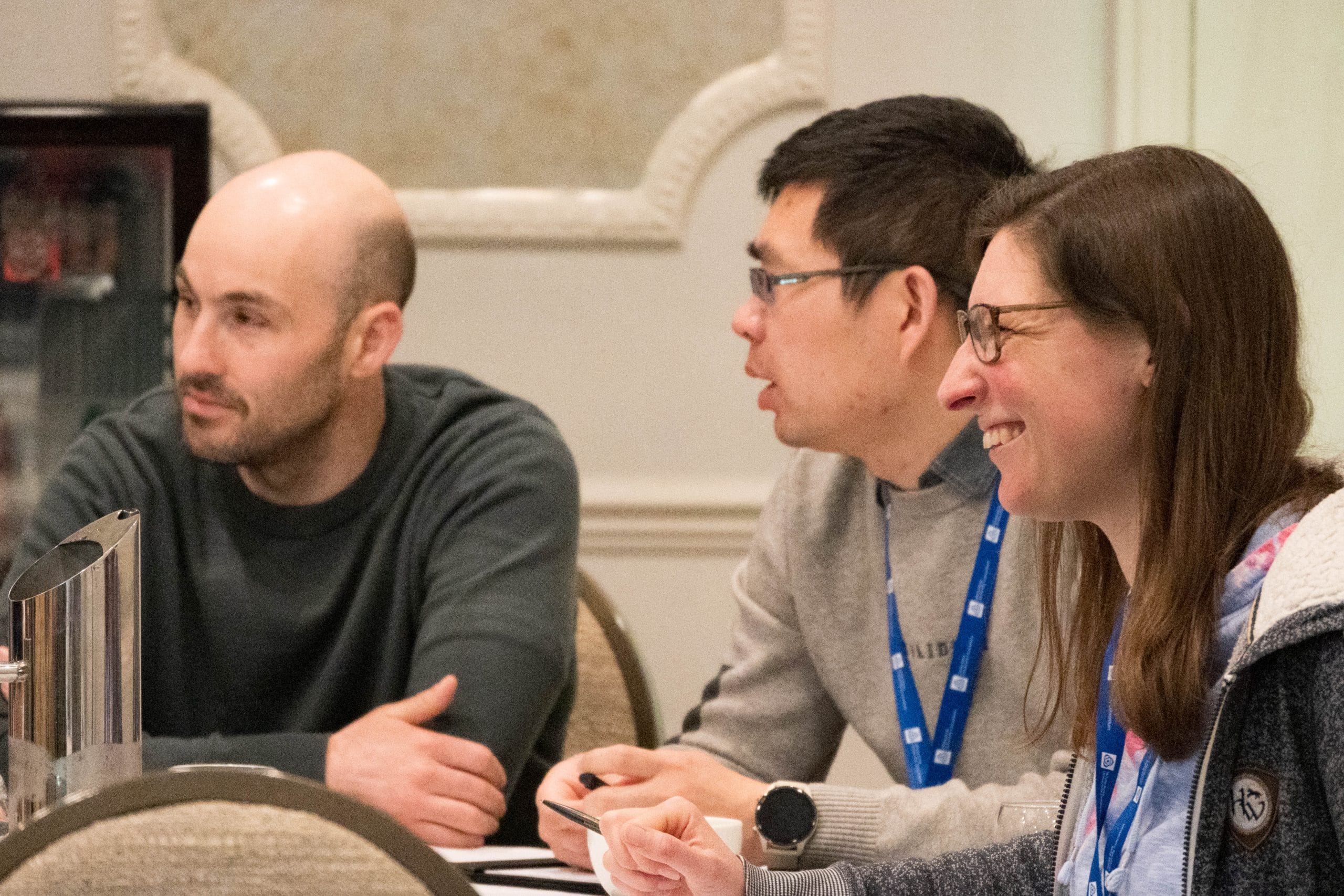 Two men and a woman sat around a table wearing lanyards and smiling