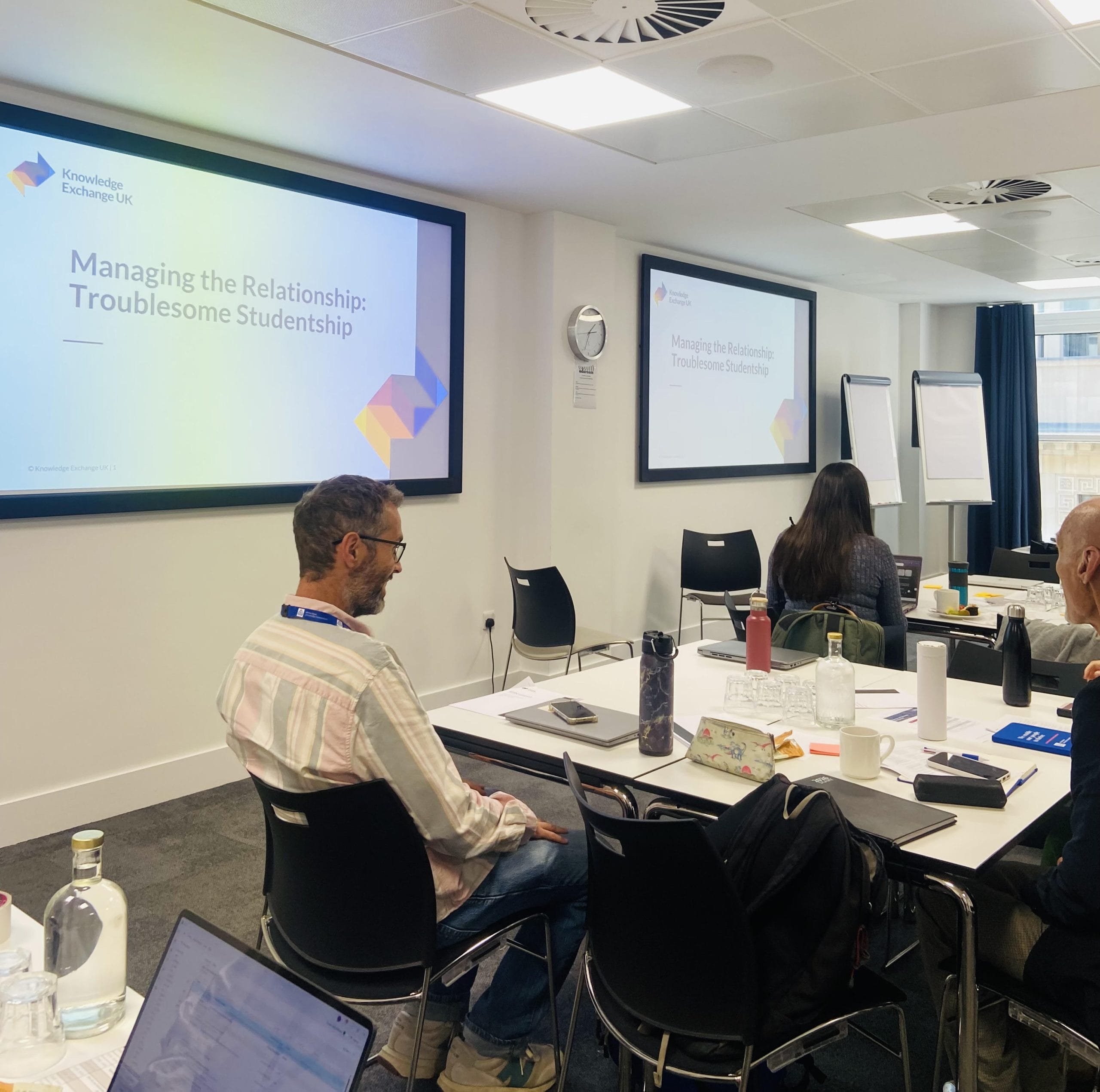 Busy room with laptops on tables and slide deck on projector