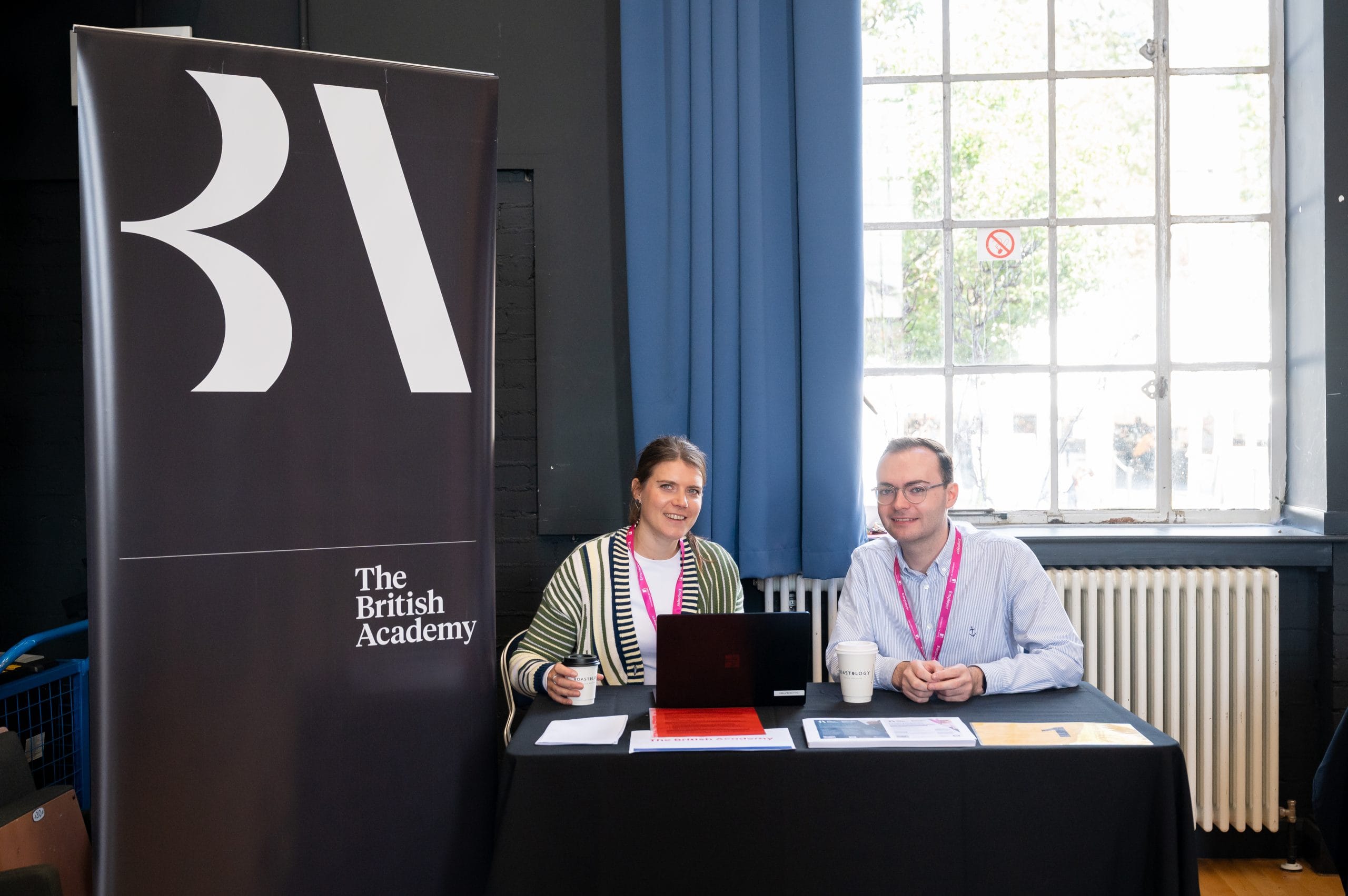 Two people smiling in front of a banner that reads 'British Academy