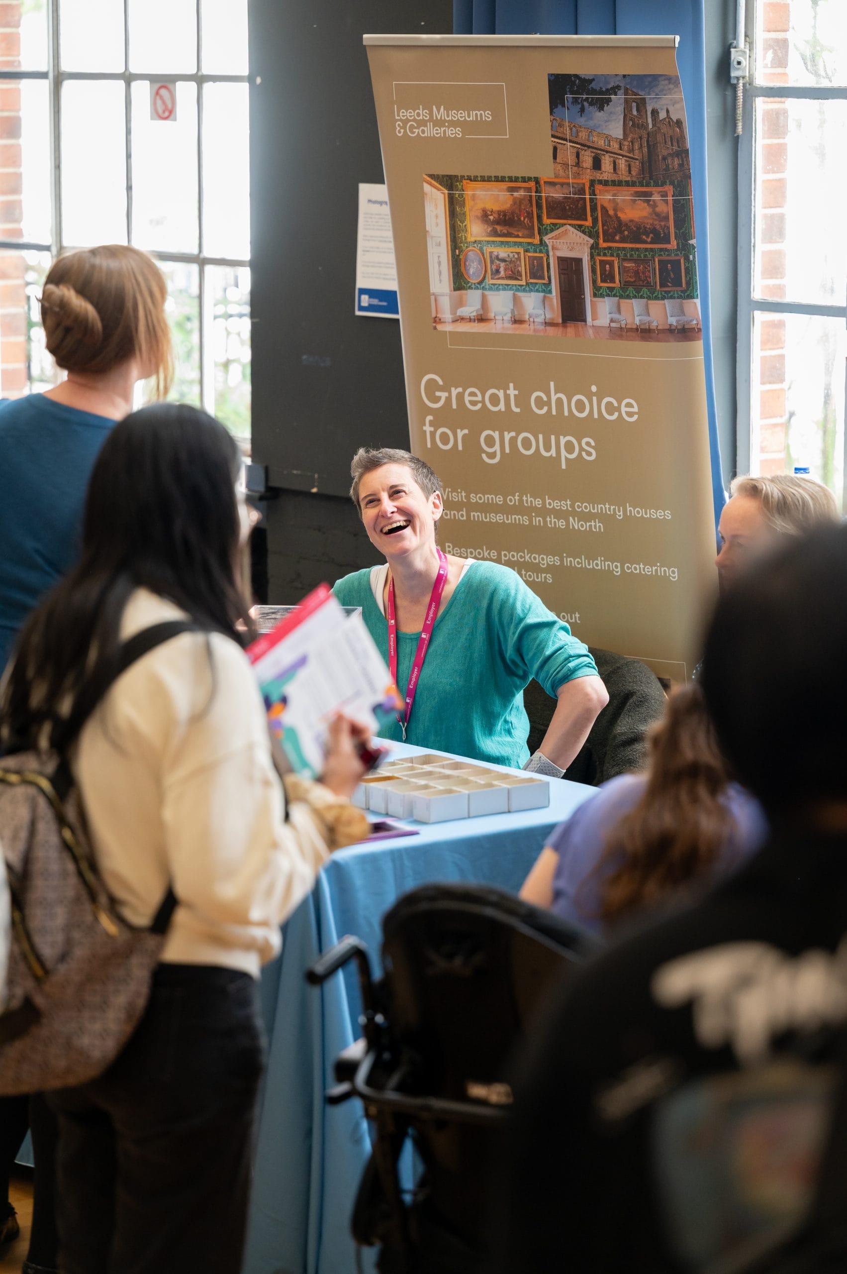 Woman laughs in front of a banner that represents 'Leeds Museums & Galleries'
