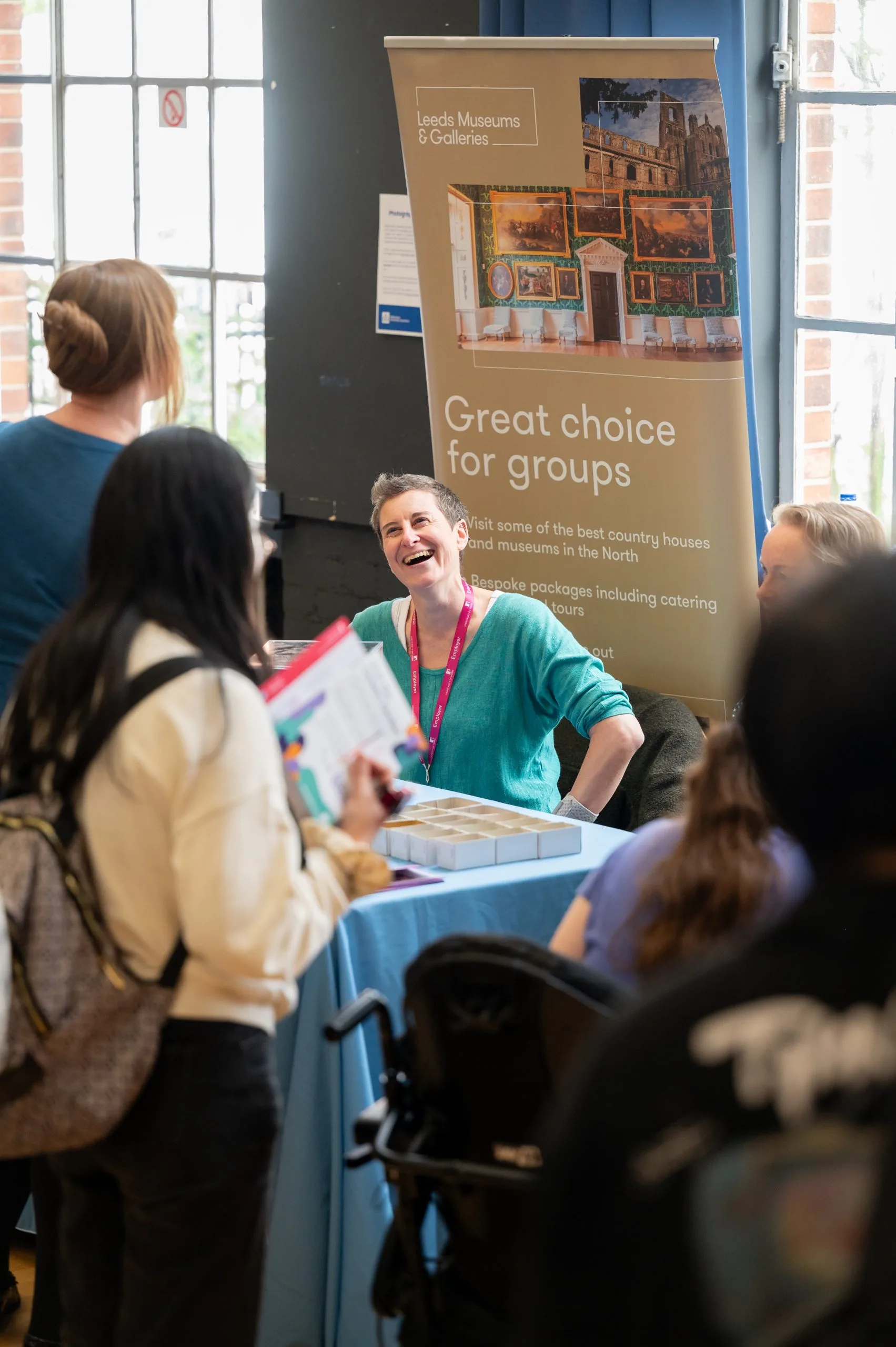 Woman laughs in front of a banner that represents 'Leeds Museums & Galleries'