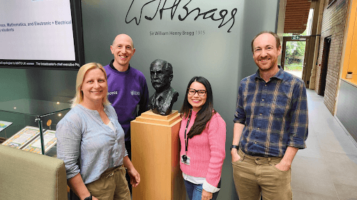 4 people smile in front of a bust of Sir William Henry Bragg